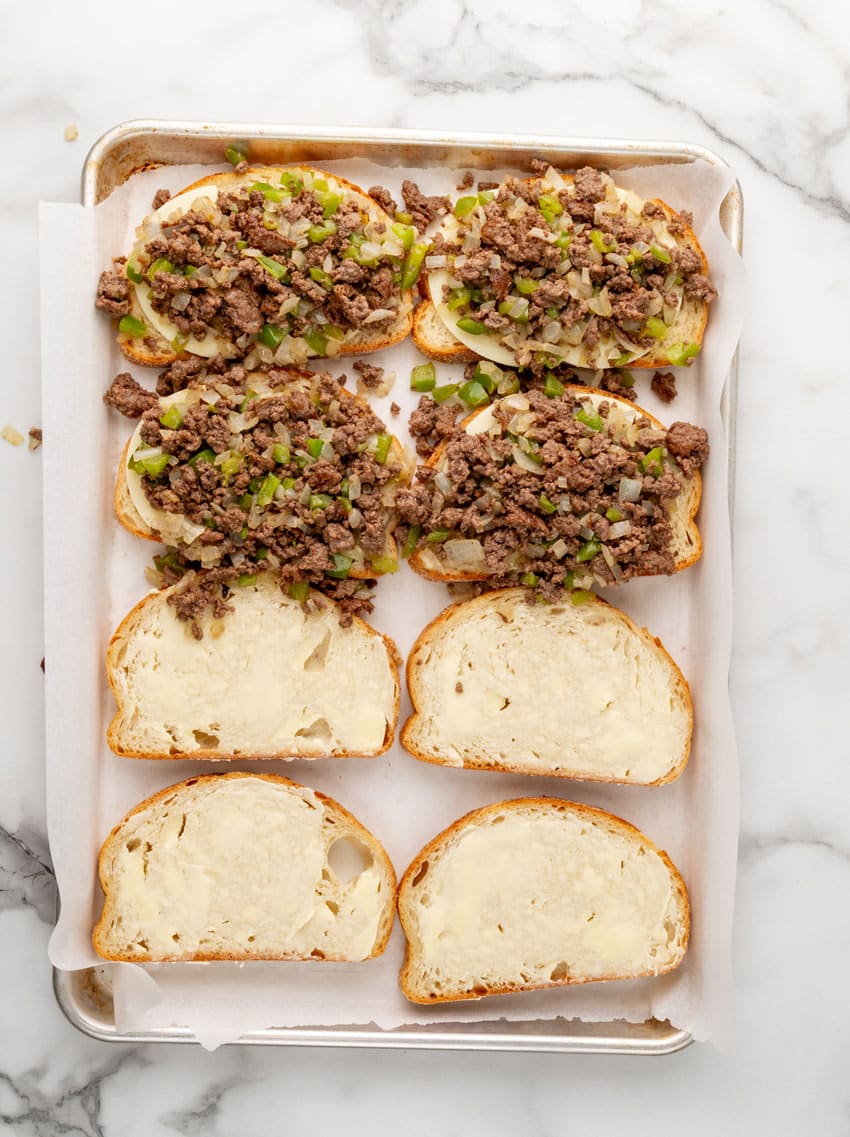 sauteed ground beef with peppers and onions on buttered slices of sourdough bread on a parchment paper lined baking tray