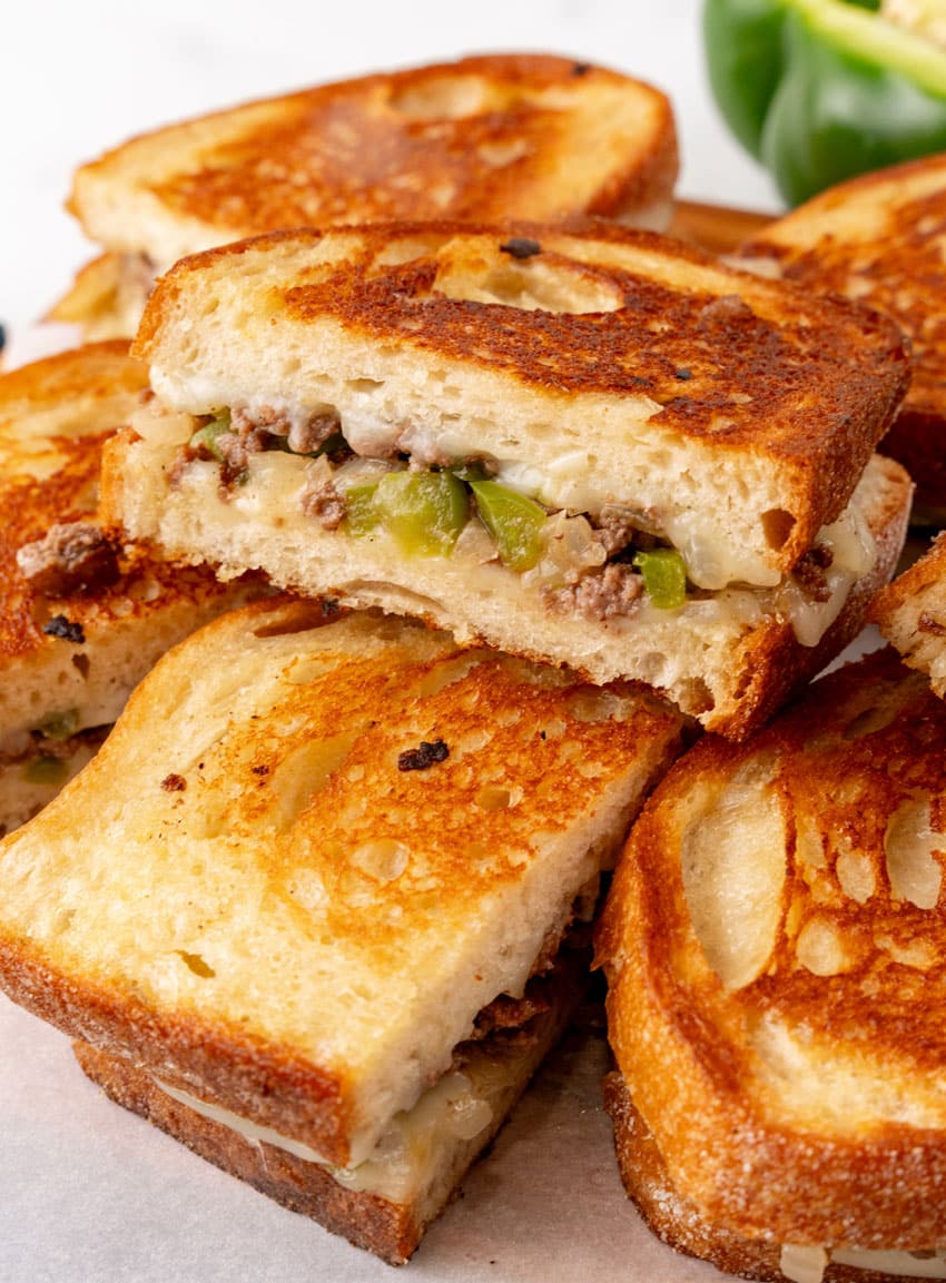 ground beef philly cheesesteak grilled cheese sandwiches on a parchment paper lined wooden cutting board