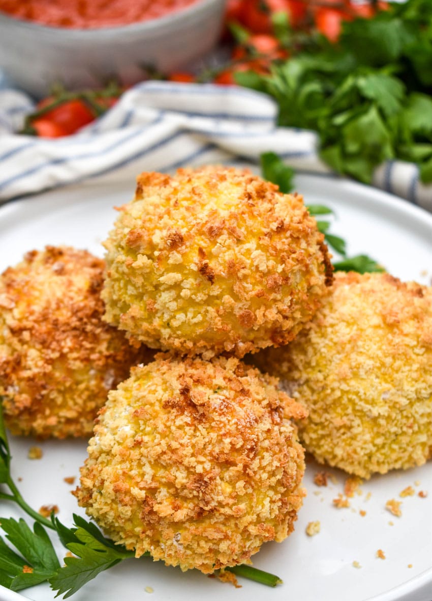 air fryer arancini rice balls stacked on a white plate with fresh herbs on the side
