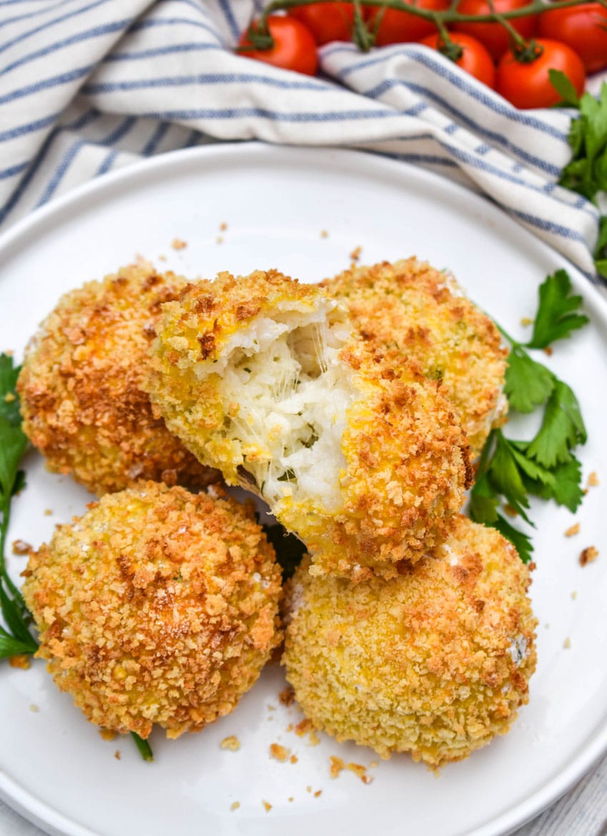 air fryer arancini rice balls stacked on a white plate with fresh herbs on the side