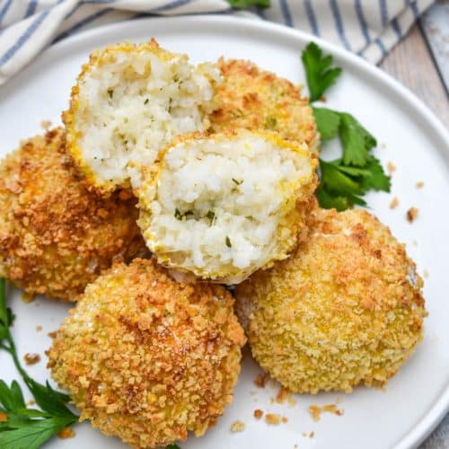 air fryer arancini rice balls stacked on a white plate with fresh herbs on the side