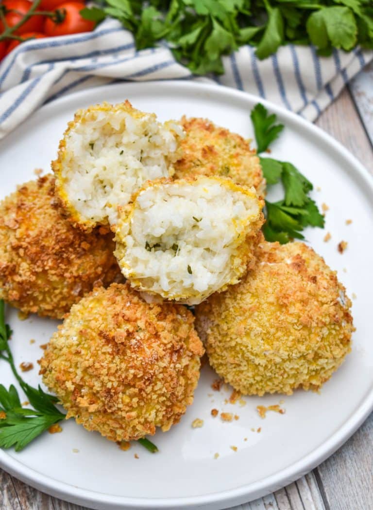 air fryer arancini rice balls stacked on a white plate with fresh herbs on the side