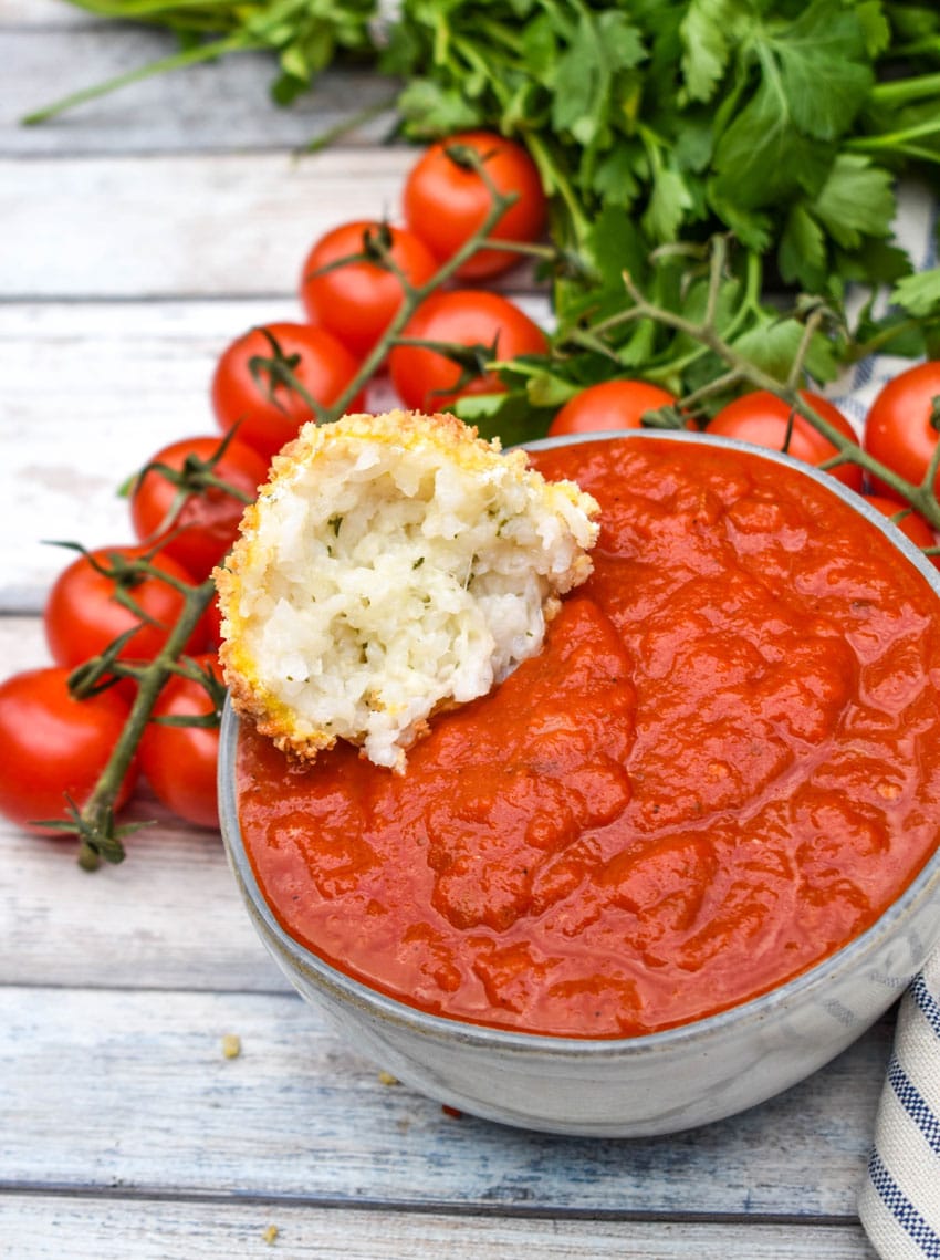 half an air fryer arancini ball resting in a small bowl of marinara sauce