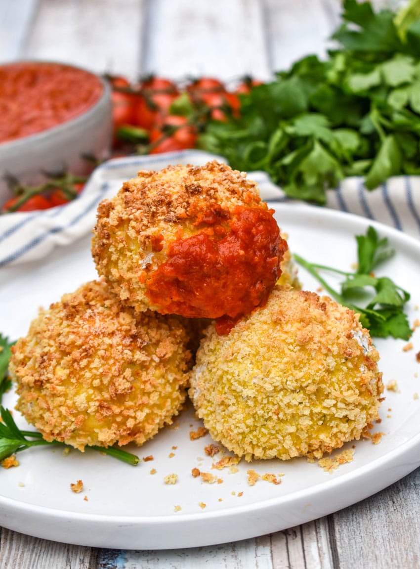 air fryer arancini rice balls stacked on a white plate with fresh herbs on the side