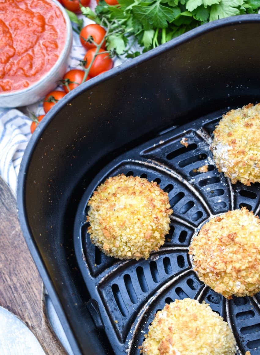 crispy panko bread crumb coated cheesy rice balls in the basket of an air fryer