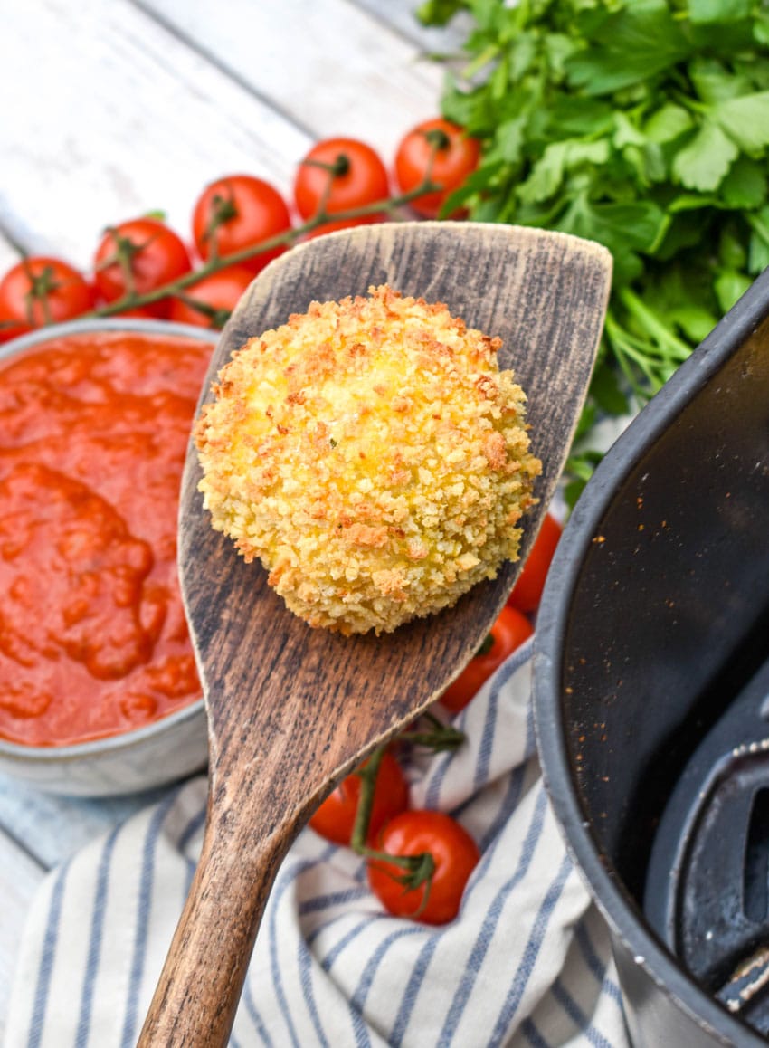 a wooden spatula holding up an air fryer arancini rice ball