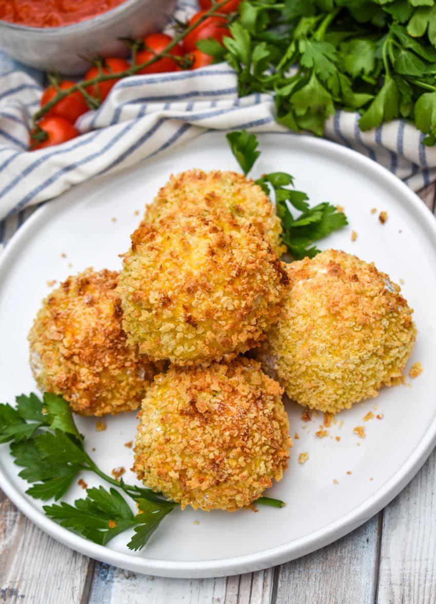 air fryer arancini rice balls stacked on a white plate with fresh herbs on the side
