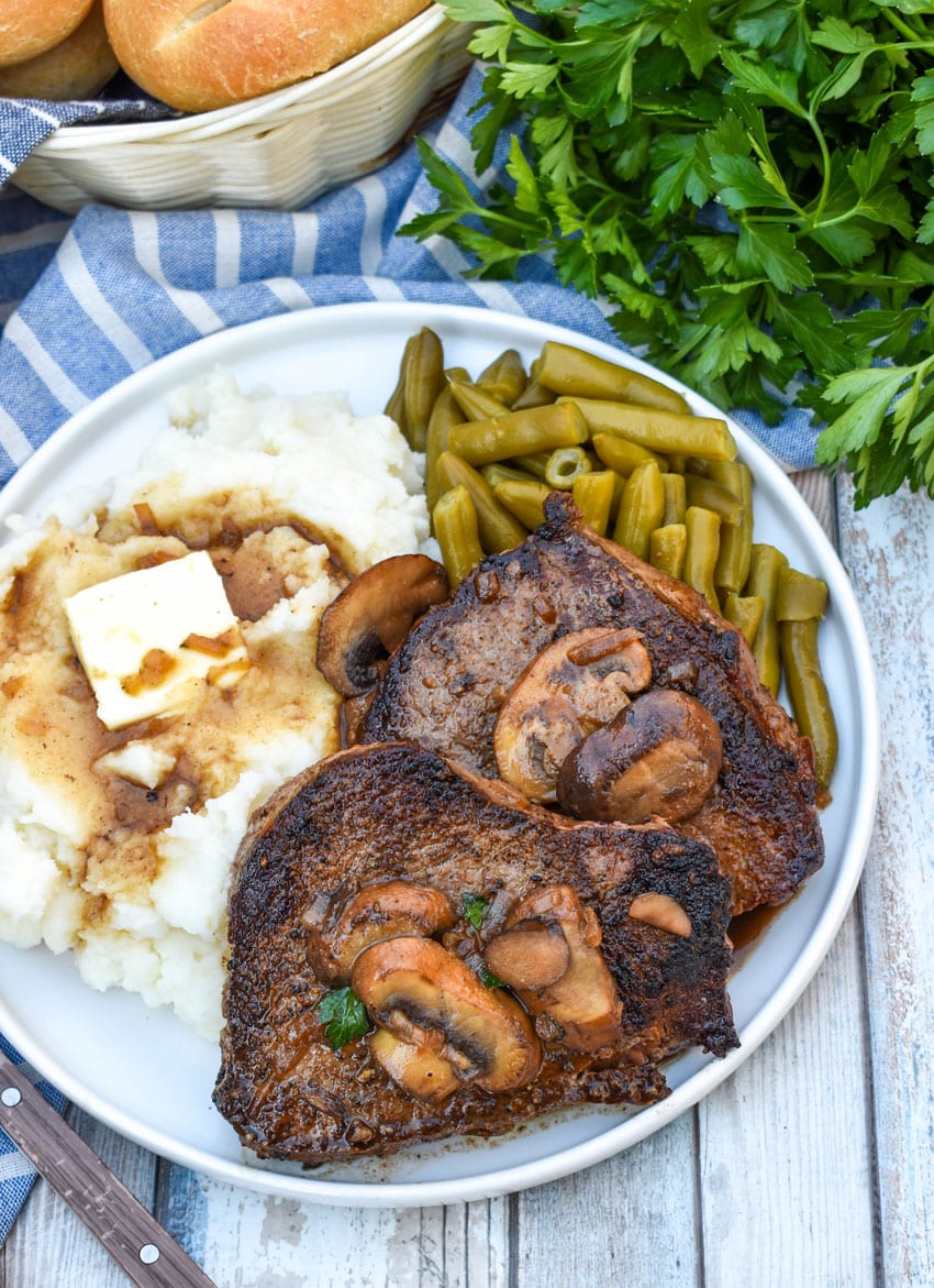 two pieces of copycat Carrabba’s Steak Marsala next to mashed potatoes and green beans on a white plate