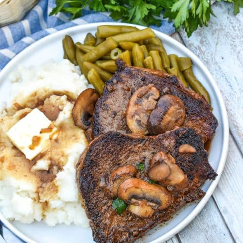 two pieces of copycat Carrabba’s Steak Marsala next to mashed potatoes and green beans on a white plate