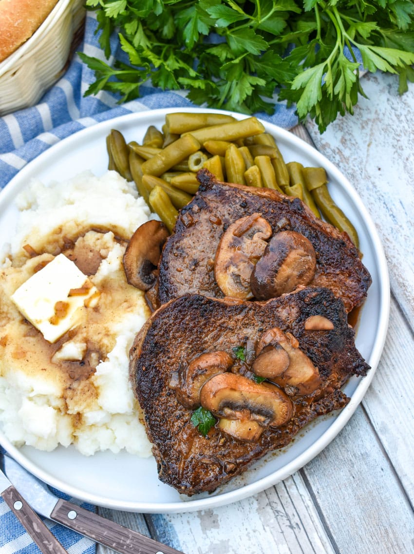 two pieces of copycat Carrabba’s Steak Marsala next to mashed potatoes and green beans on a white plate