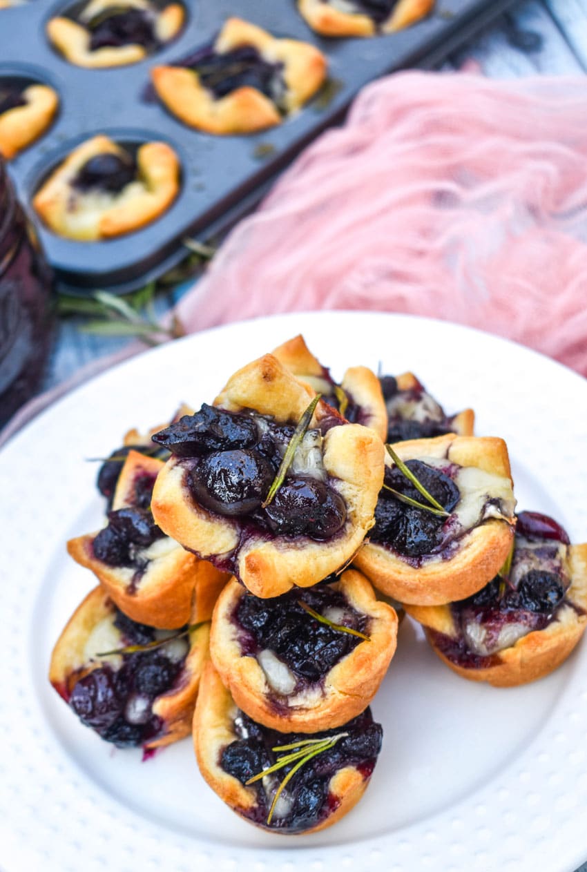 a close up of cranberry brie bites stacked on a white serving plate