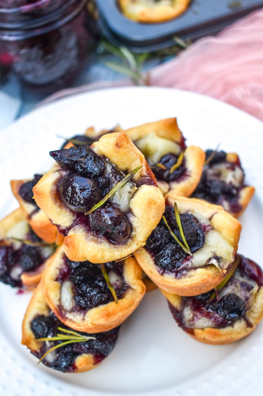 a close up of cranberry brie bites stacked on a white serving plate