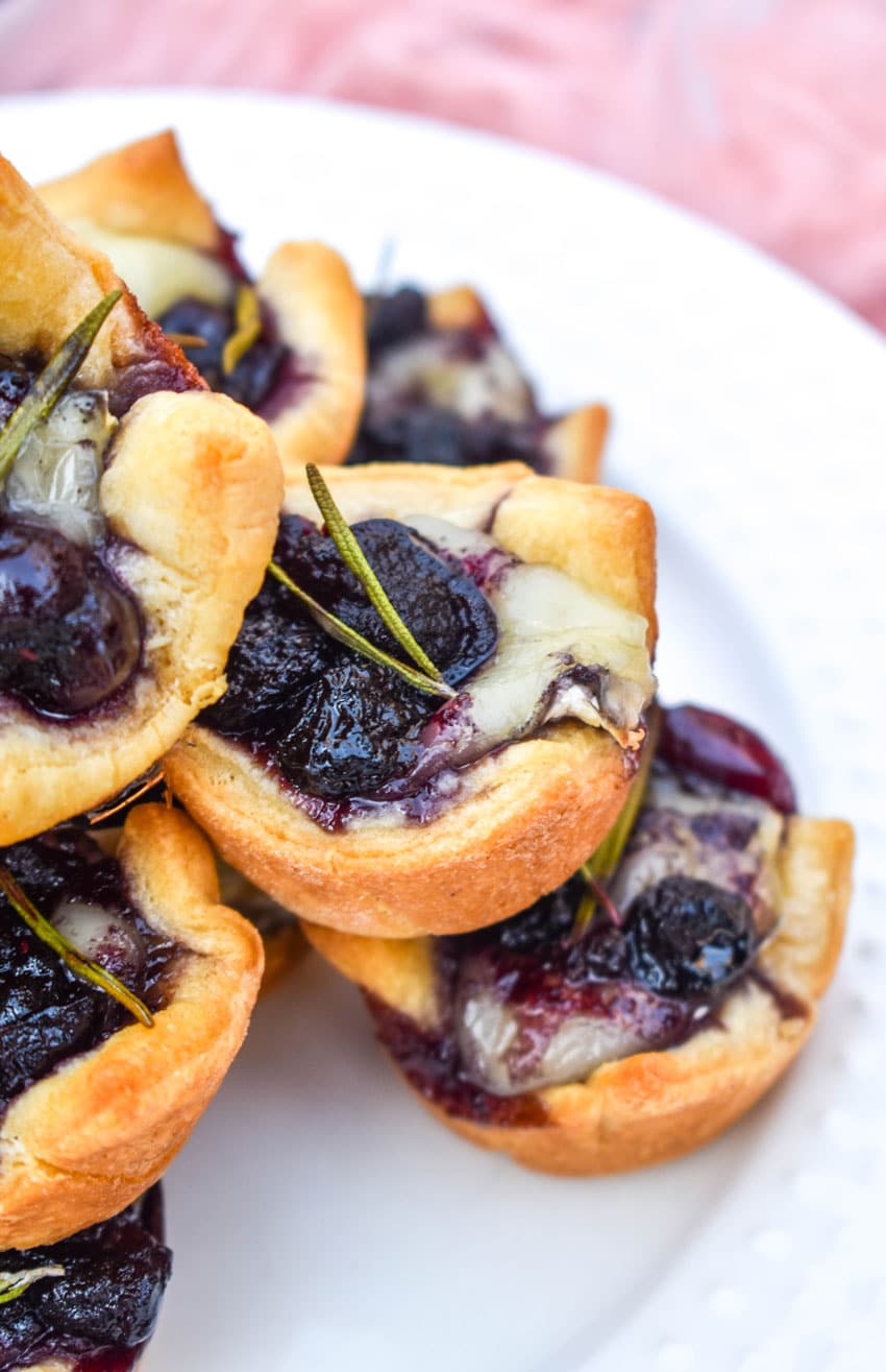a close up of cranberry brie bites stacked on a white serving plate