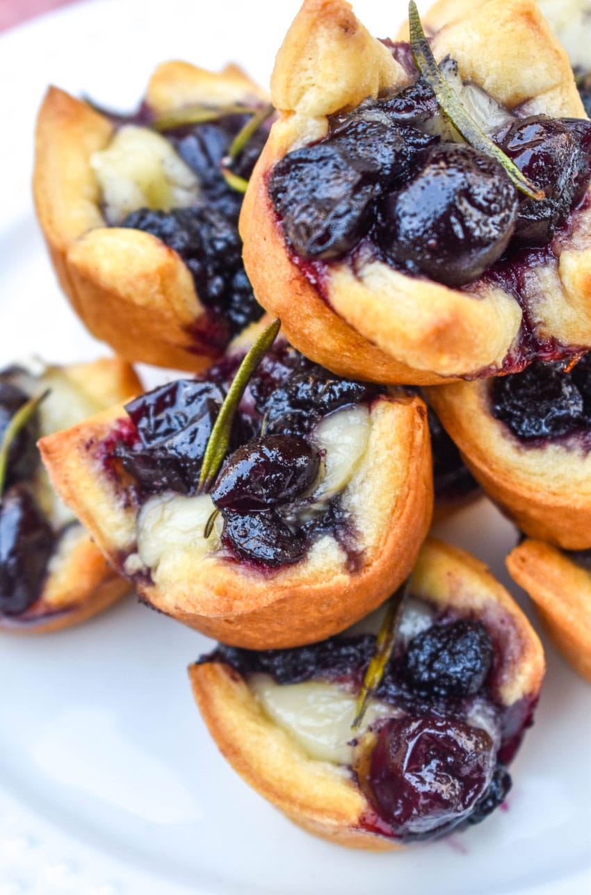 a close up of cranberry brie bites stacked on a white serving plate