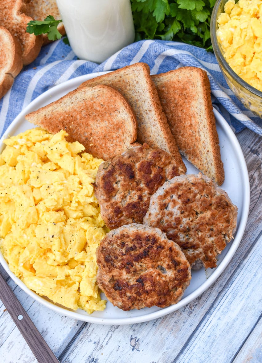 homemade breakfast sausage patties next to scrambled eggs and toast on a white plate