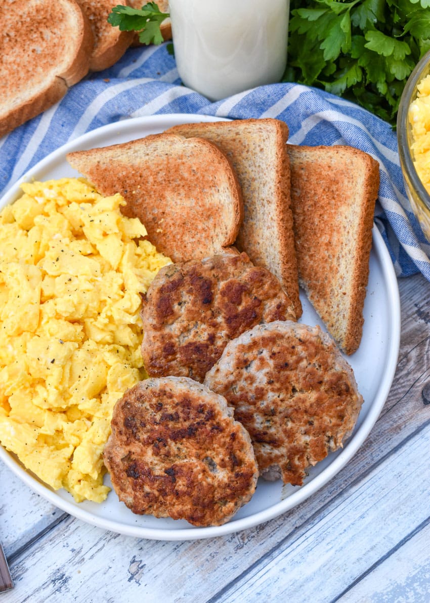 homemade breakfast sausage patties next to scrambled eggs and toast on a white plate