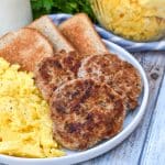 homemade breakfast sausage patties next to scrambled eggs and toast on a white plate