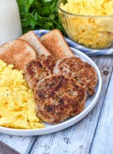 homemade breakfast sausage patties next to scrambled eggs and toast on a white plate