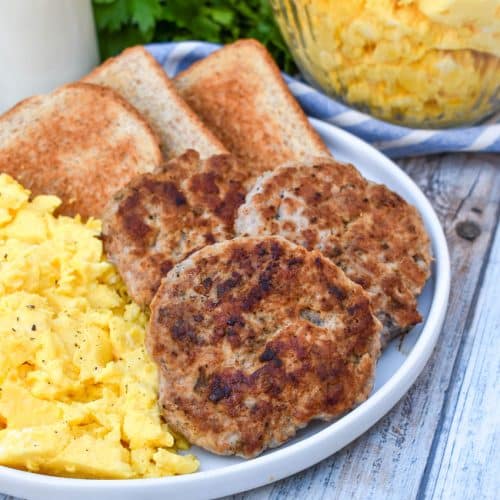 homemade breakfast sausage patties next to scrambled eggs and toast on a white plate