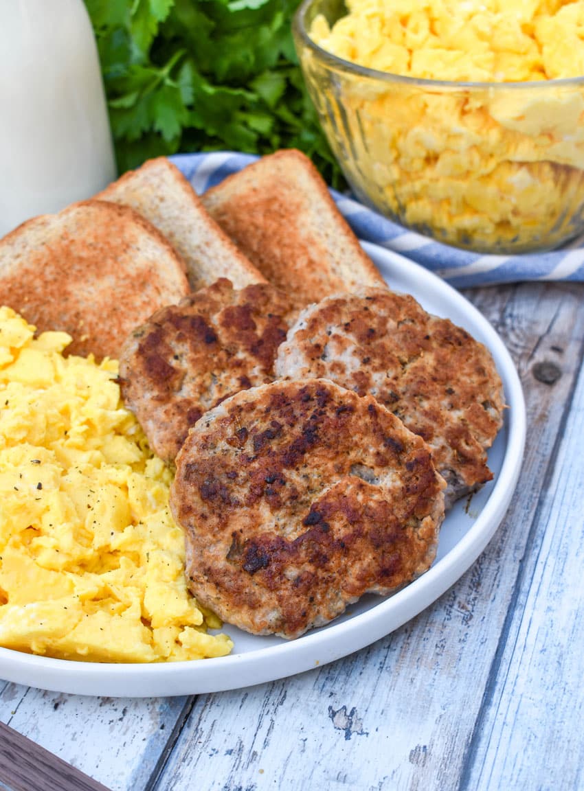 homemade breakfast sausage patties next to scrambled eggs and toast on a white plate