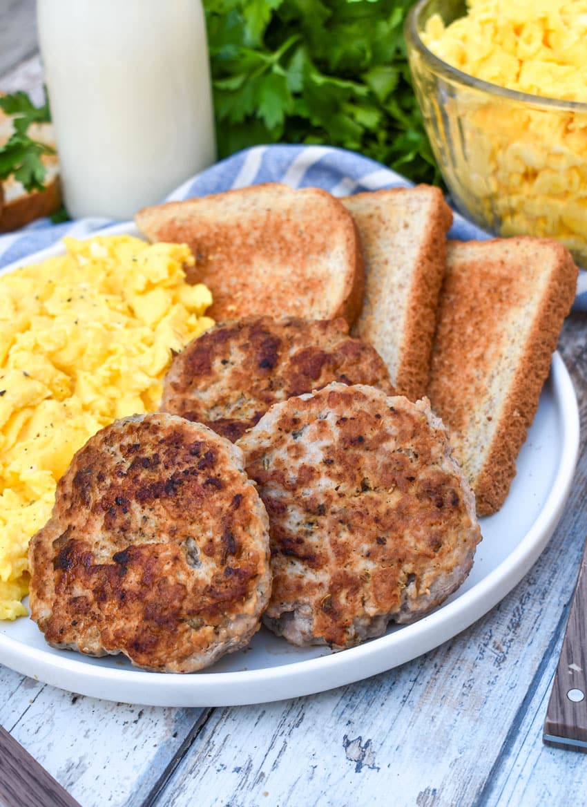 homemade breakfast sausage patties next to scrambled eggs and toast on a white plate