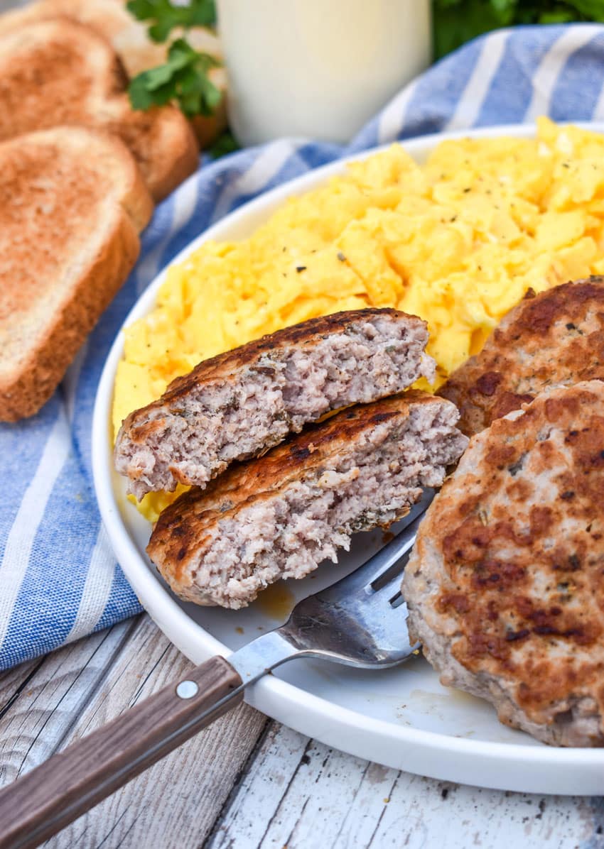 homemade breakfast sausage patties next to scrambled eggs and toast on a white plate