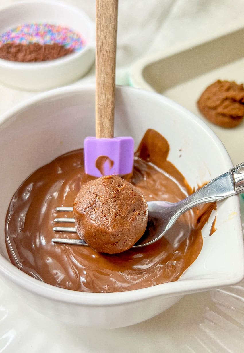 a fork holding a naked brownie cheesecake truffle over a bowl of melted chocolate