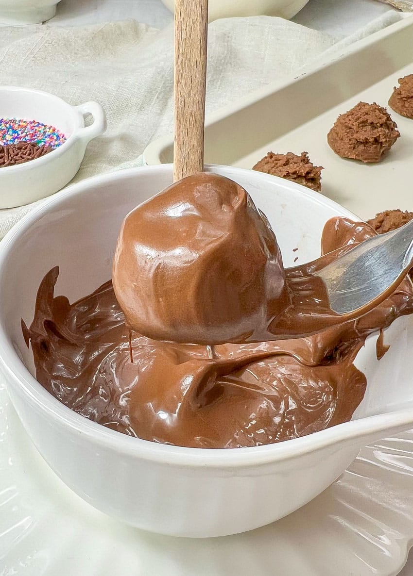 a fork holding a brownie cheesecake truffle over a bowl of melted chocolate