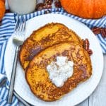 two slices of pumpkin french toast topped with syrup and a dollop of whipped cream on a small white plate with a silver fork resting on the edge
