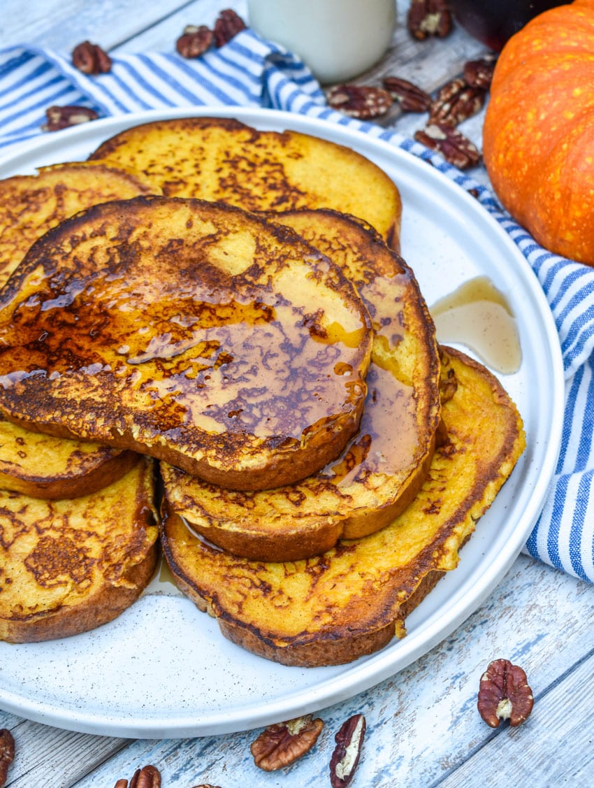 syrup topped slices of pumpkin french toast stacked on a large white plate