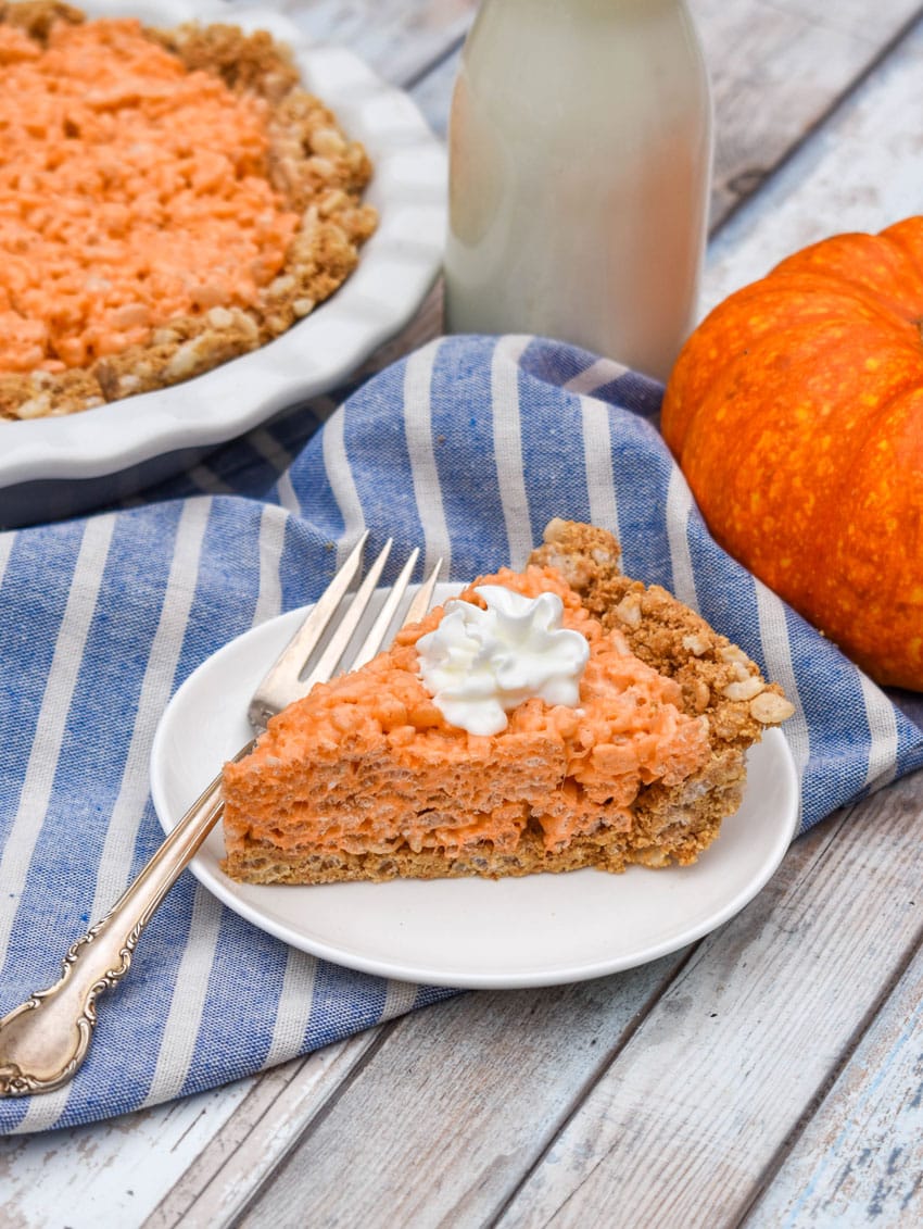 a slice of a pumpkin pie rice krispie treat topped with whipped cream on a small white dessert plate with a silver fork resting on the side