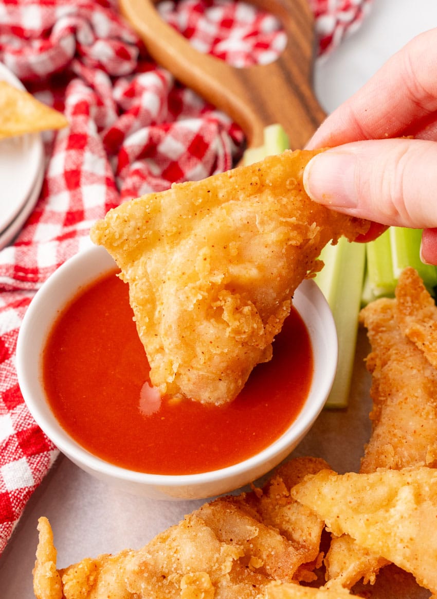 a hand dipping a fried buffalo blast into a small bowl of hot sauce