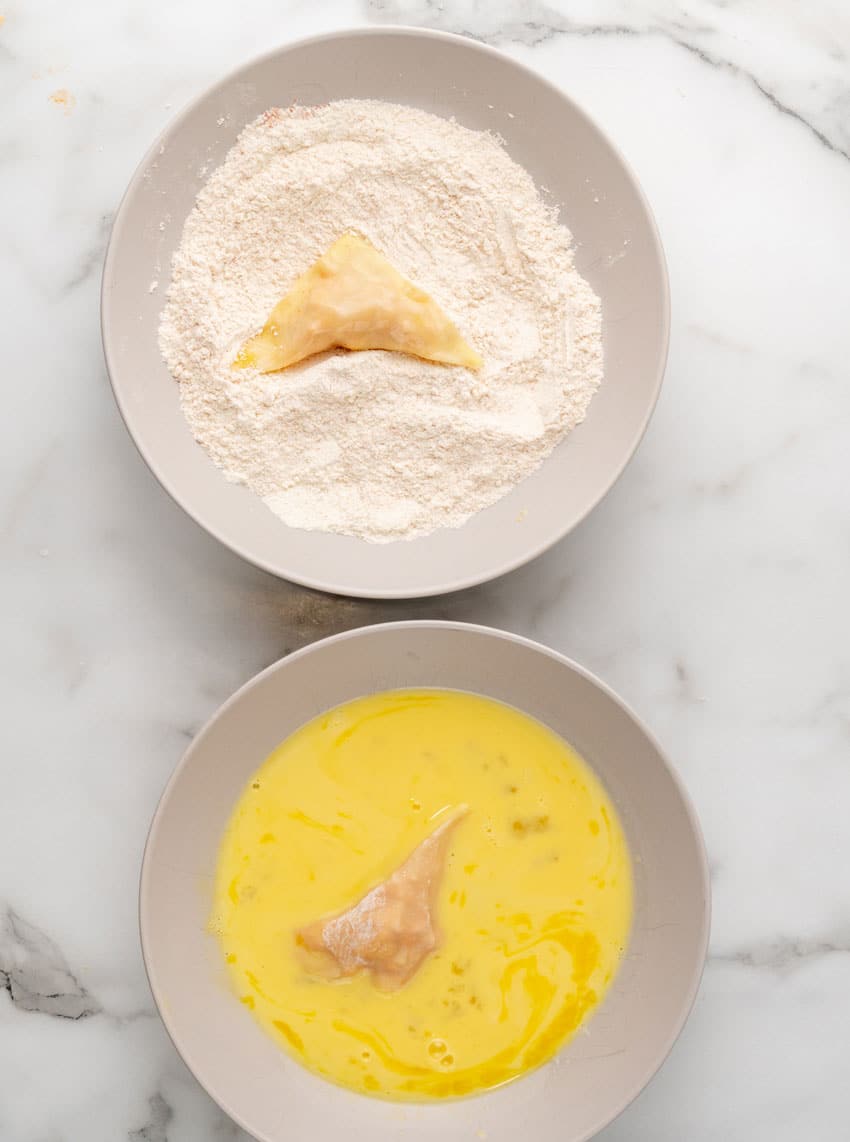 buffalo chicken filled wonton wrappers being dredged in flour and dipped in beaten egg