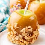 a homemade caramel apple coated in crushed peanuts on a small white dessert plate