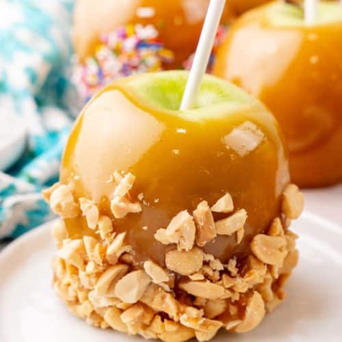 a homemade caramel apple coated in crushed peanuts on a small white dessert plate