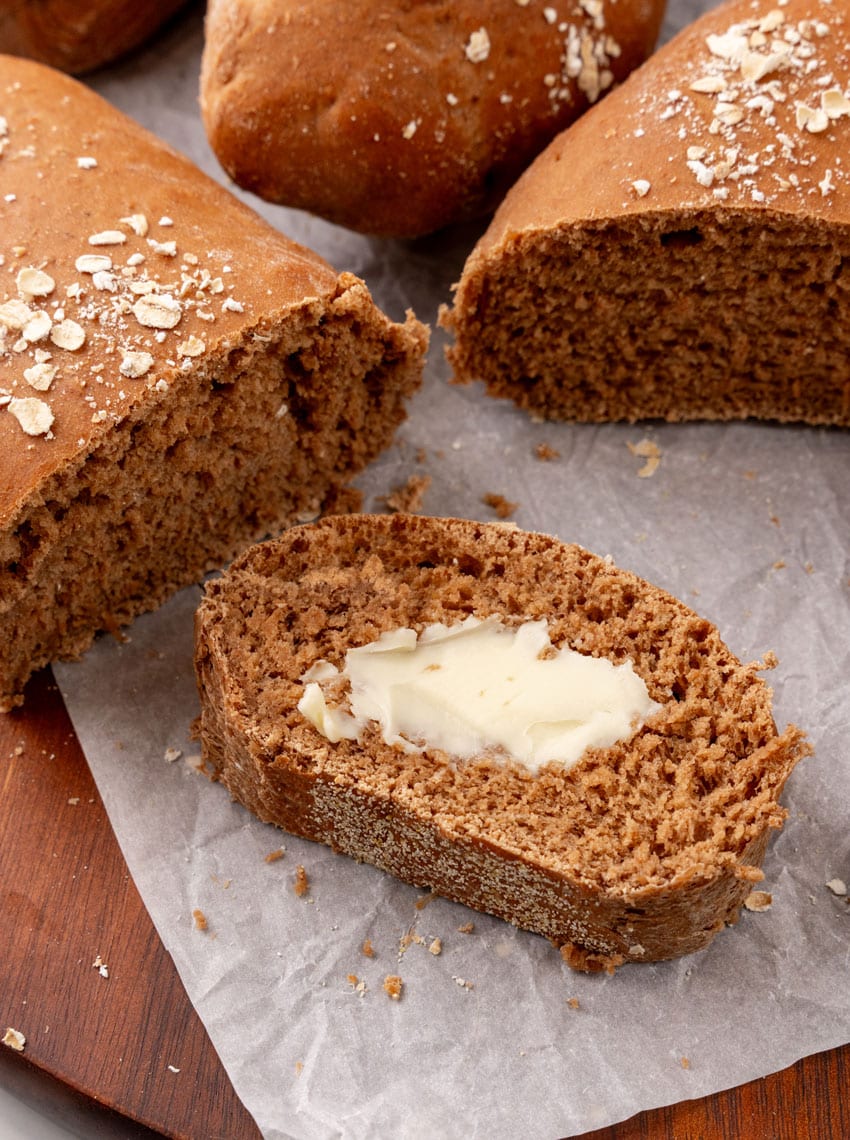 a slice of copycat cheesecake factory brown bread spread with softened butter on a parchment paper lined wooden serving tray