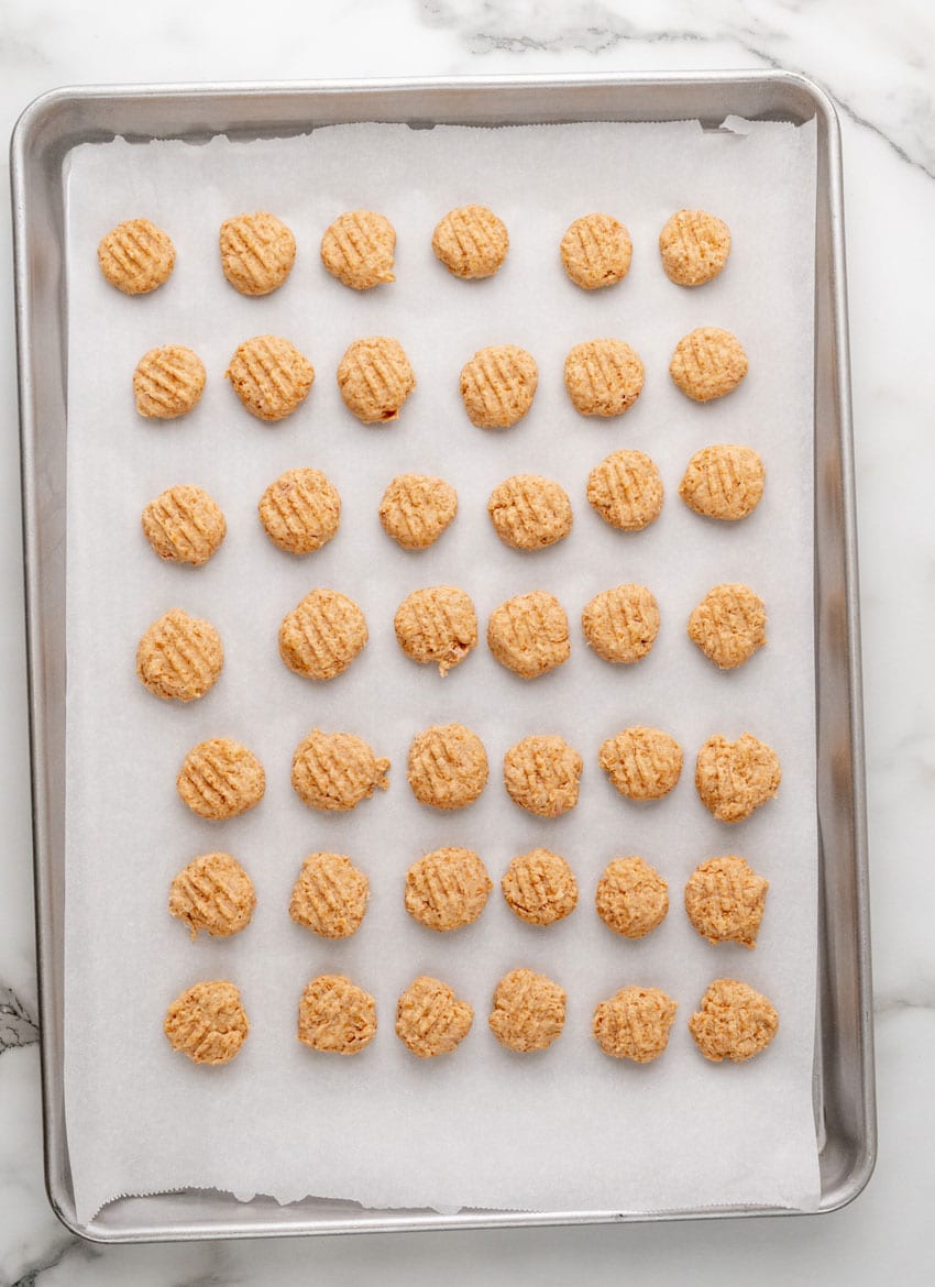 unbaked homemade cat treats arranged in rows on a parchment paper lined baking sheet