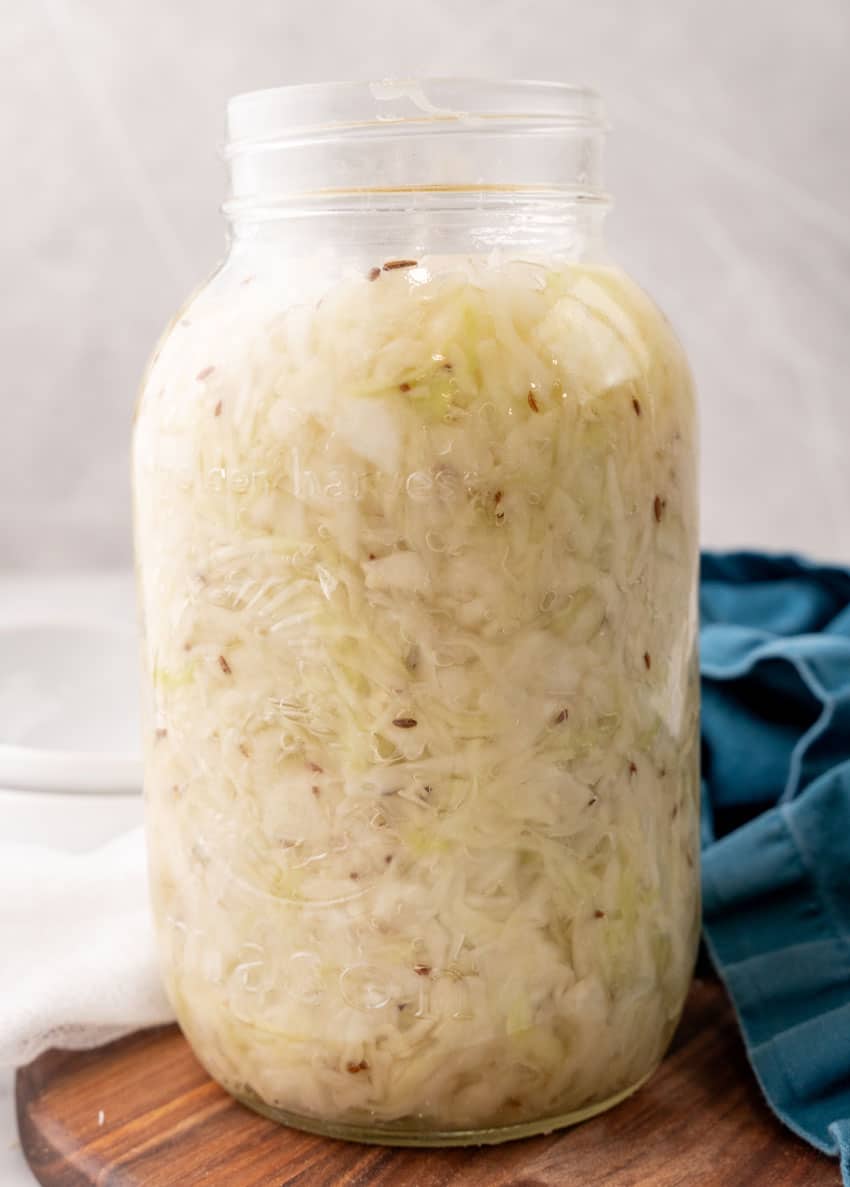 easy homemade sauerkraut in a large glass jar sitting on a wooden tray