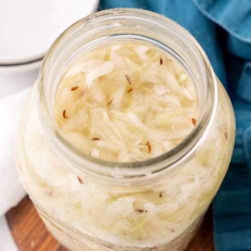 easy homemade sauerkraut in a large glass jar sitting on a wooden tray