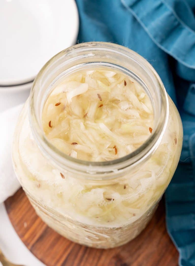 easy homemade sauerkraut in a large glass jar sitting on a wooden tray