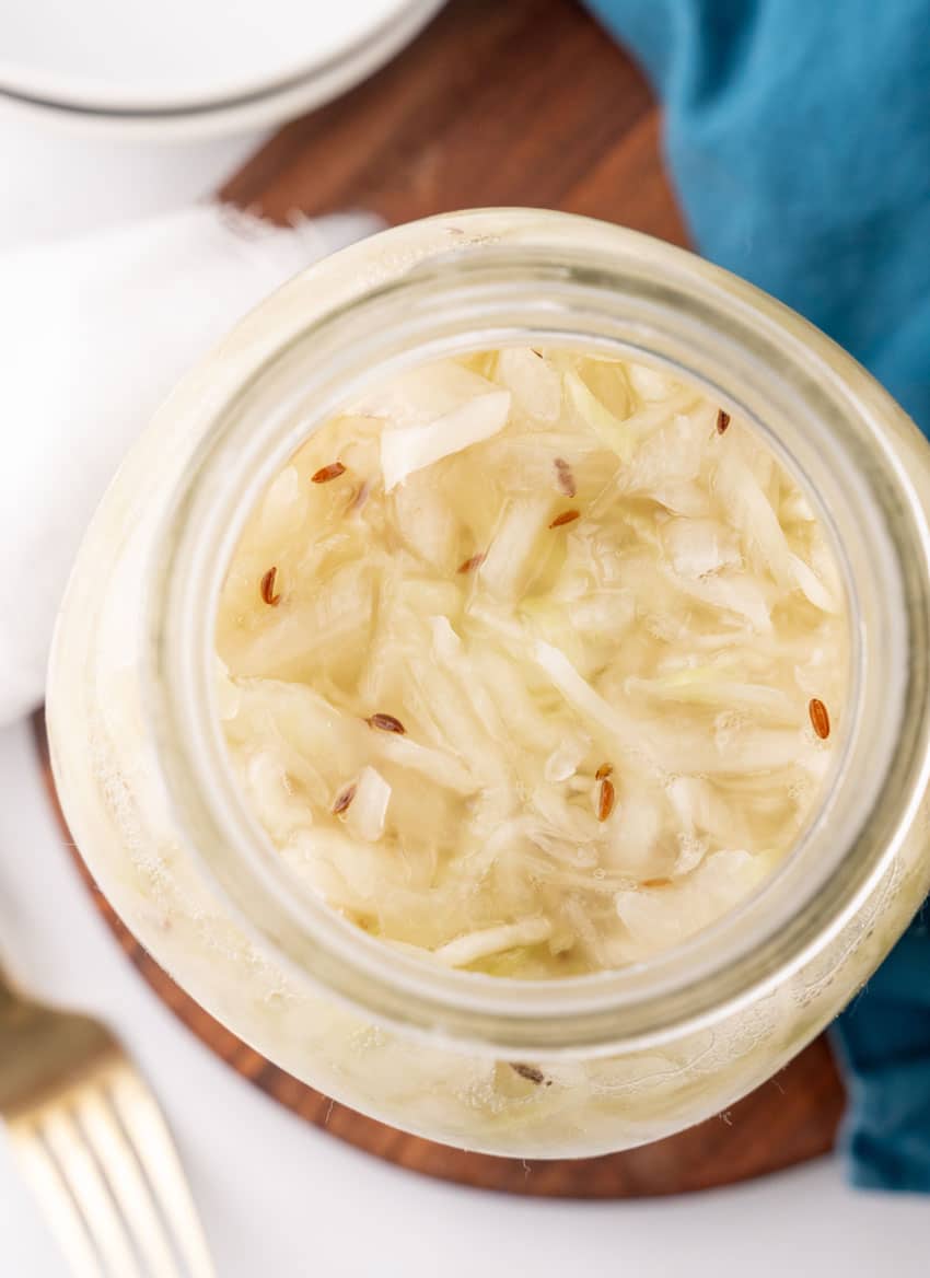 easy homemade sauerkraut in a large glass jar sitting on a wooden tray