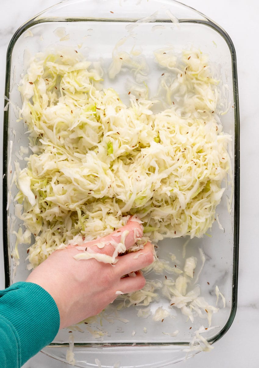 salted sliced fresh cabbage mixed with caraway seeds in a large glass baking dish