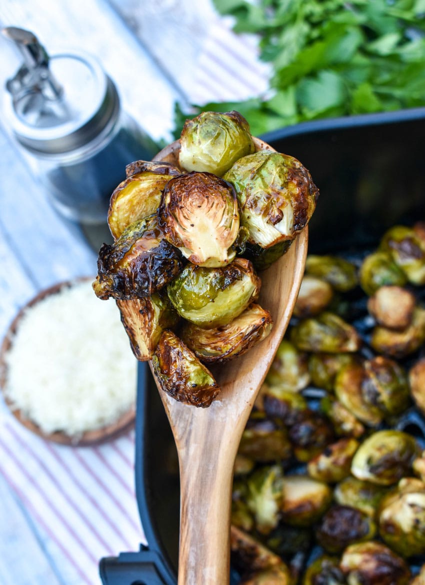 a wooden spoon holding up a scoop of air fryer balsamic roasted brussels sprouts