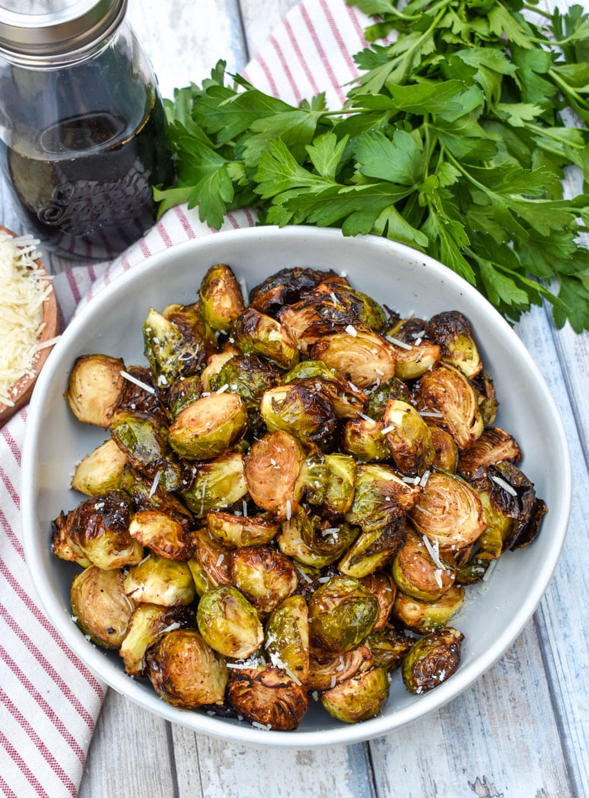 air fryer balsamic roasted brussels sprouts in a large white serving bowl with fresh herbs on the side