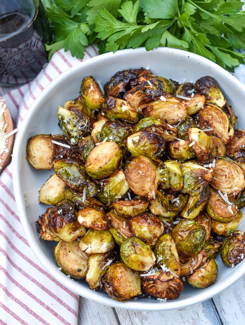 air fryer balsamic roasted brussels sprouts in a large white serving bowl with fresh herbs on the side
