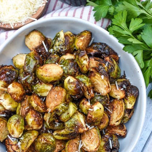 air fryer balsamic roasted brussels sprouts in a large white serving bowl with fresh herbs on the side