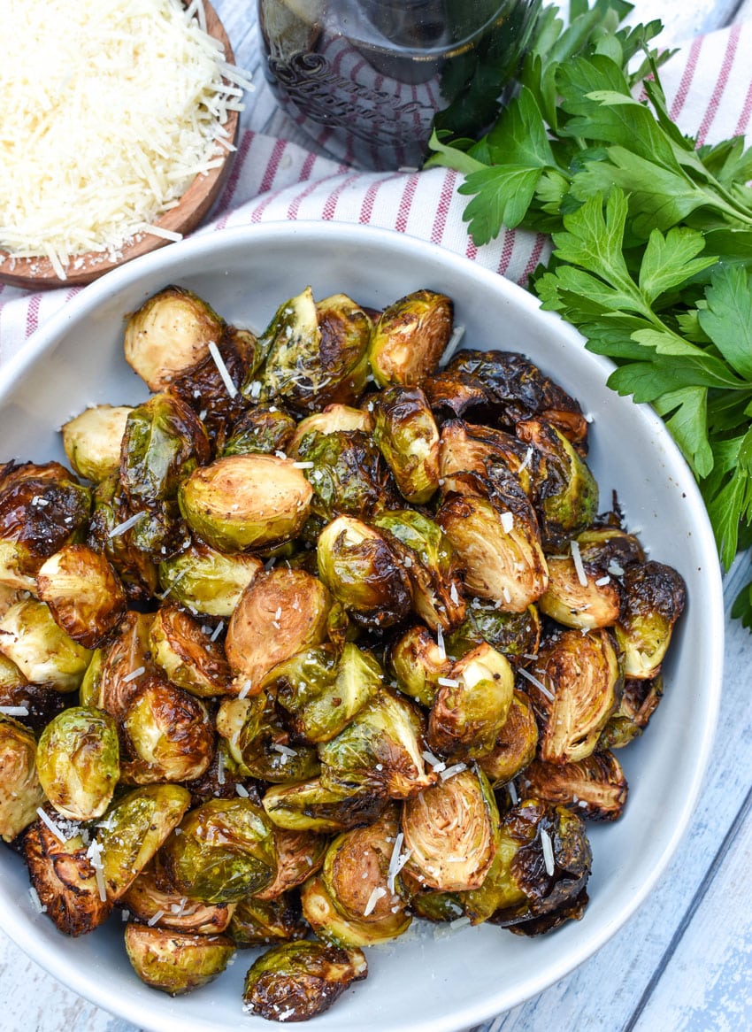 air fryer balsamic roasted brussels sprouts in a large white serving bowl with fresh herbs on the side