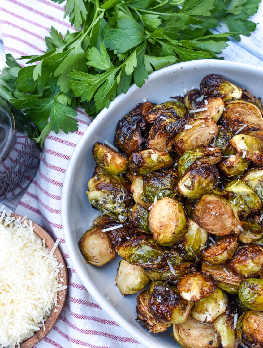air fryer balsamic roasted brussels sprouts in a large white serving bowl with fresh herbs on the side