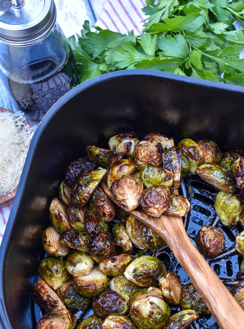 a wooden spoon scooping balsamic glazed roasted brussels sprouts out of the basket of an air fryer