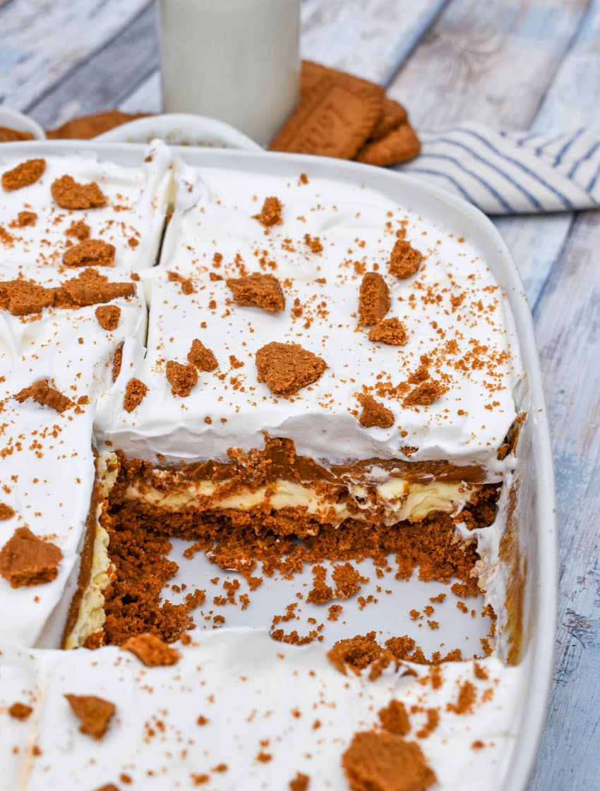 a layered cookie butter dessert in a white baking dish with a slice removed to show the inner layers